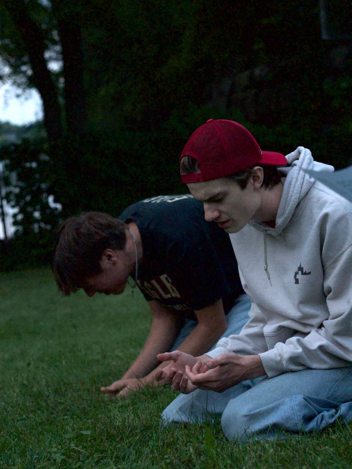Two young men kneeling in prayer outdoors at dusk