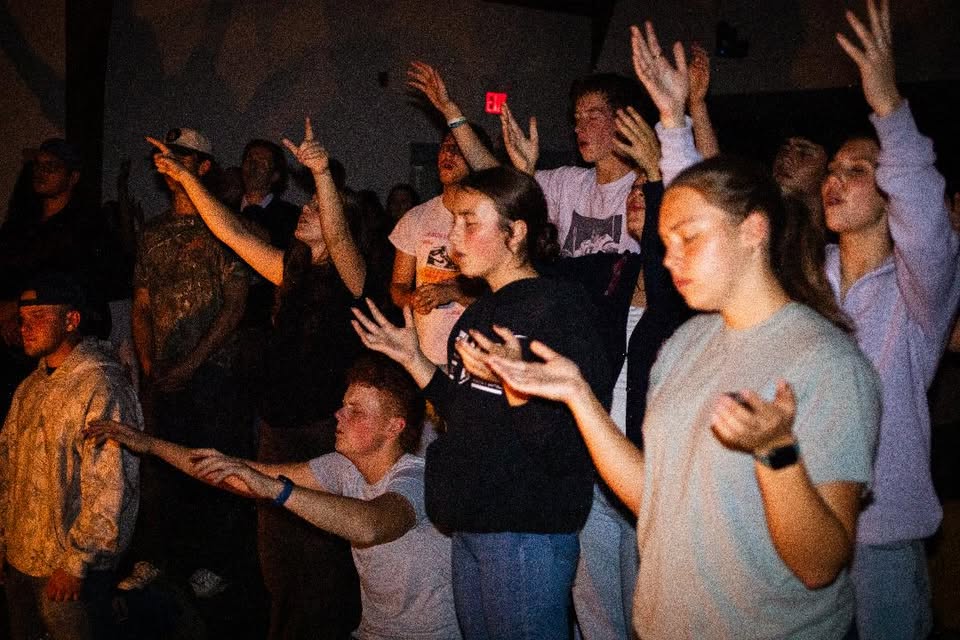 Hands lifted in worship across a room full of people pressing into God's presence