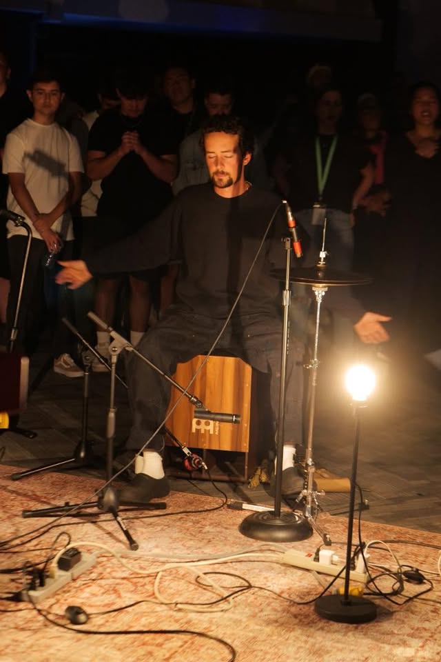 A percussionist lost in worship on cajon beneath a warm lamp