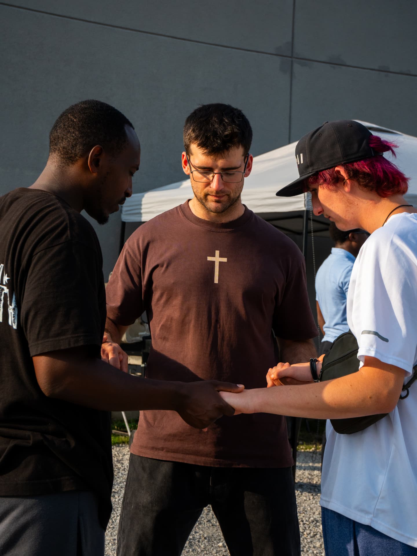 Three men holding hands in prayer at an outdoor gathering