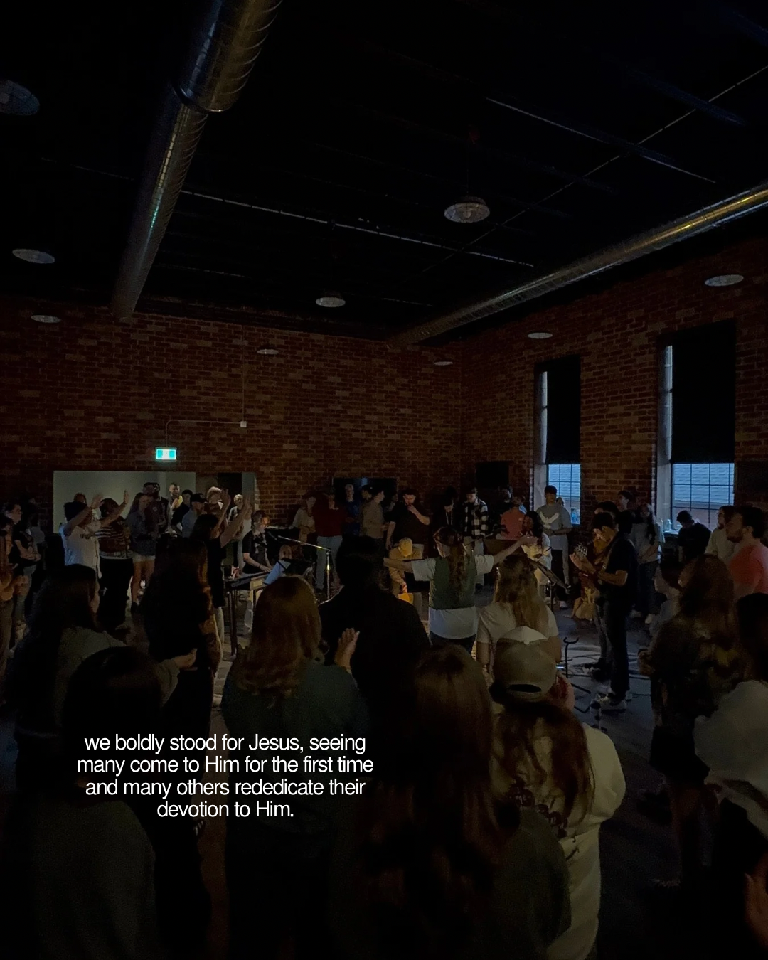 A crowd worshipping together in a brick-walled gathering space