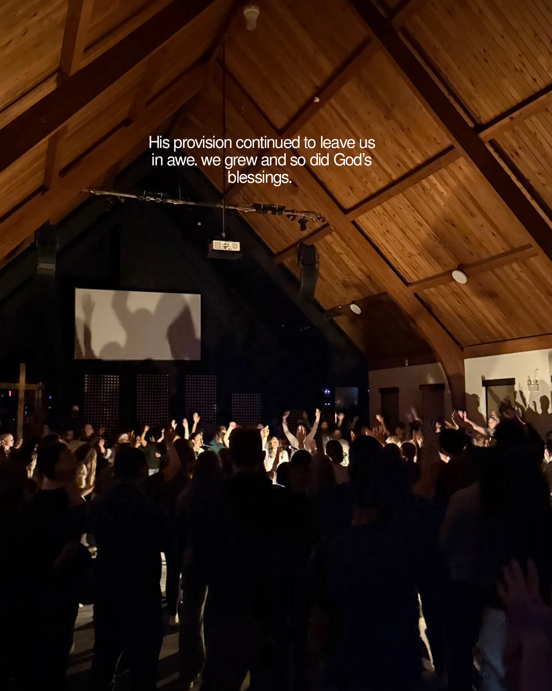 A room full of worshippers raising their hands beneath the chapel's wooden ceiling