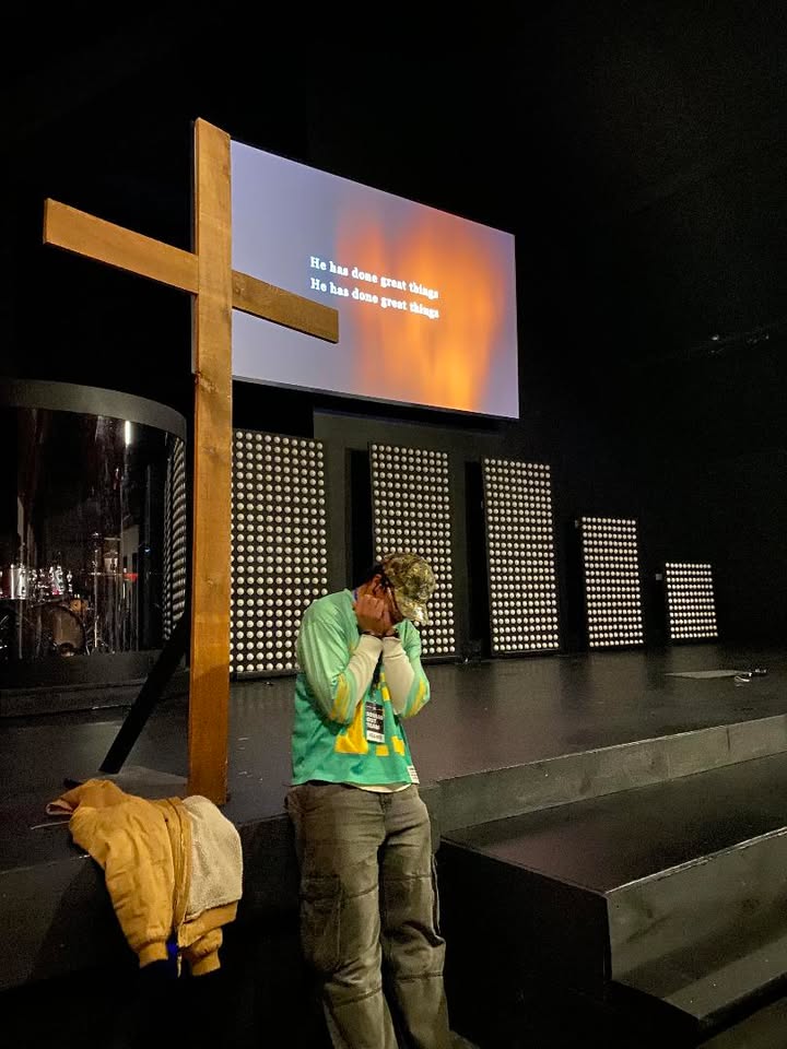 A young man surrendered in prayer at the foot of the cross as the words He has done great things fill the screen